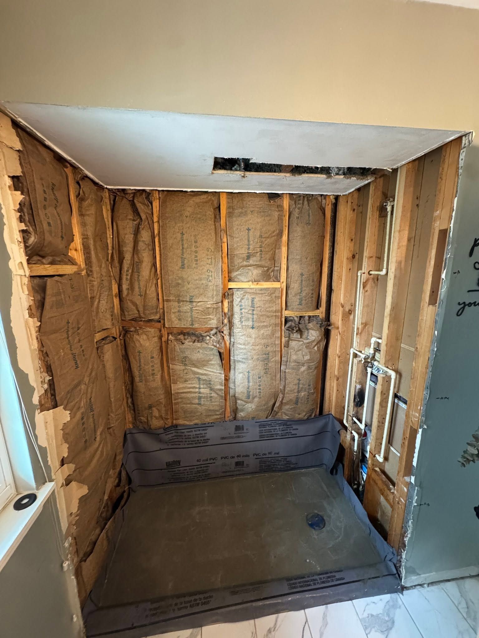 Unfinished shower alcove with exposed framing, insulation, and plumbing, awaiting wall board and tile.