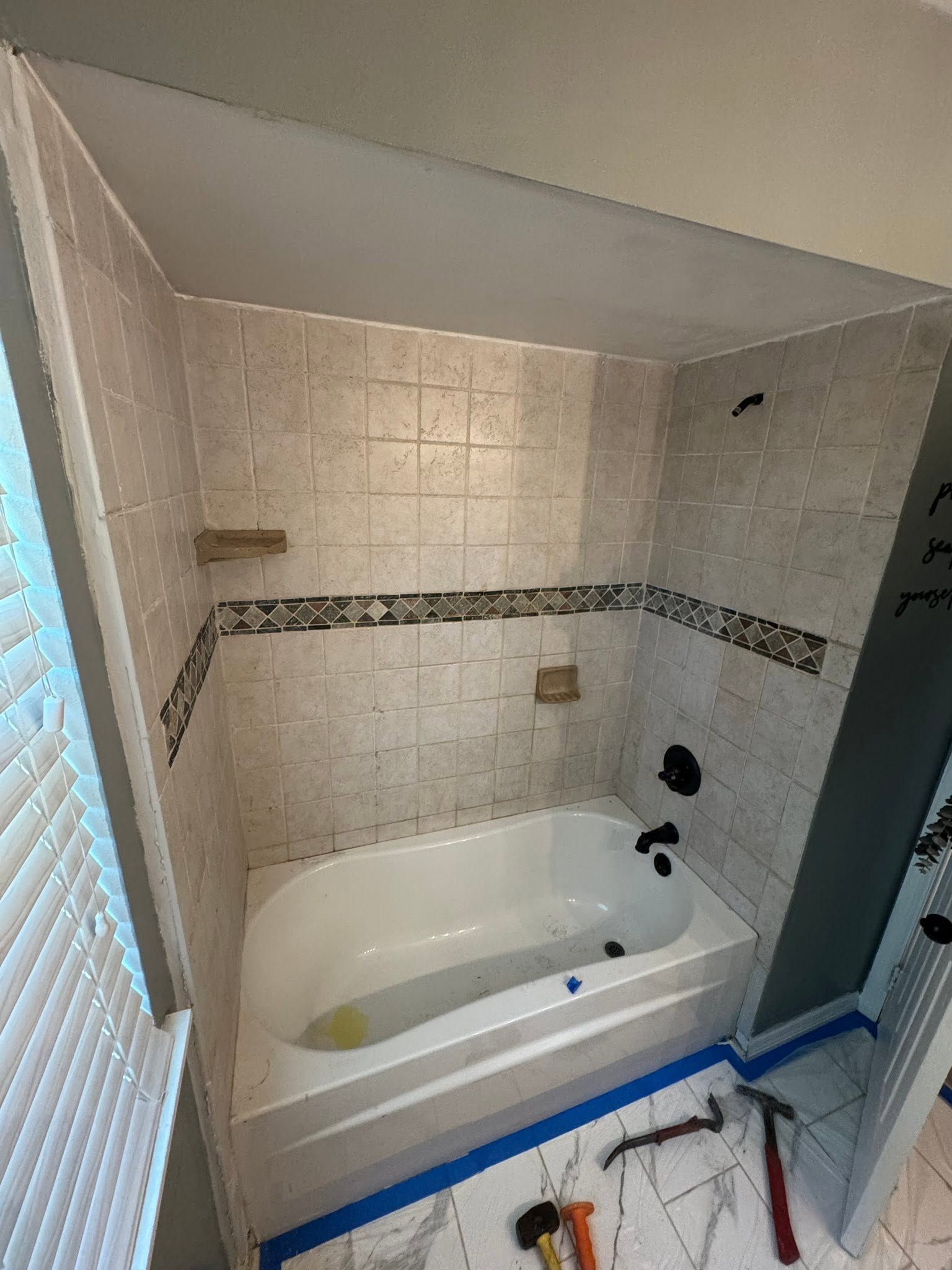 Small tiled bathroom with a white bathtub and shower fixtures, viewed from the doorway.