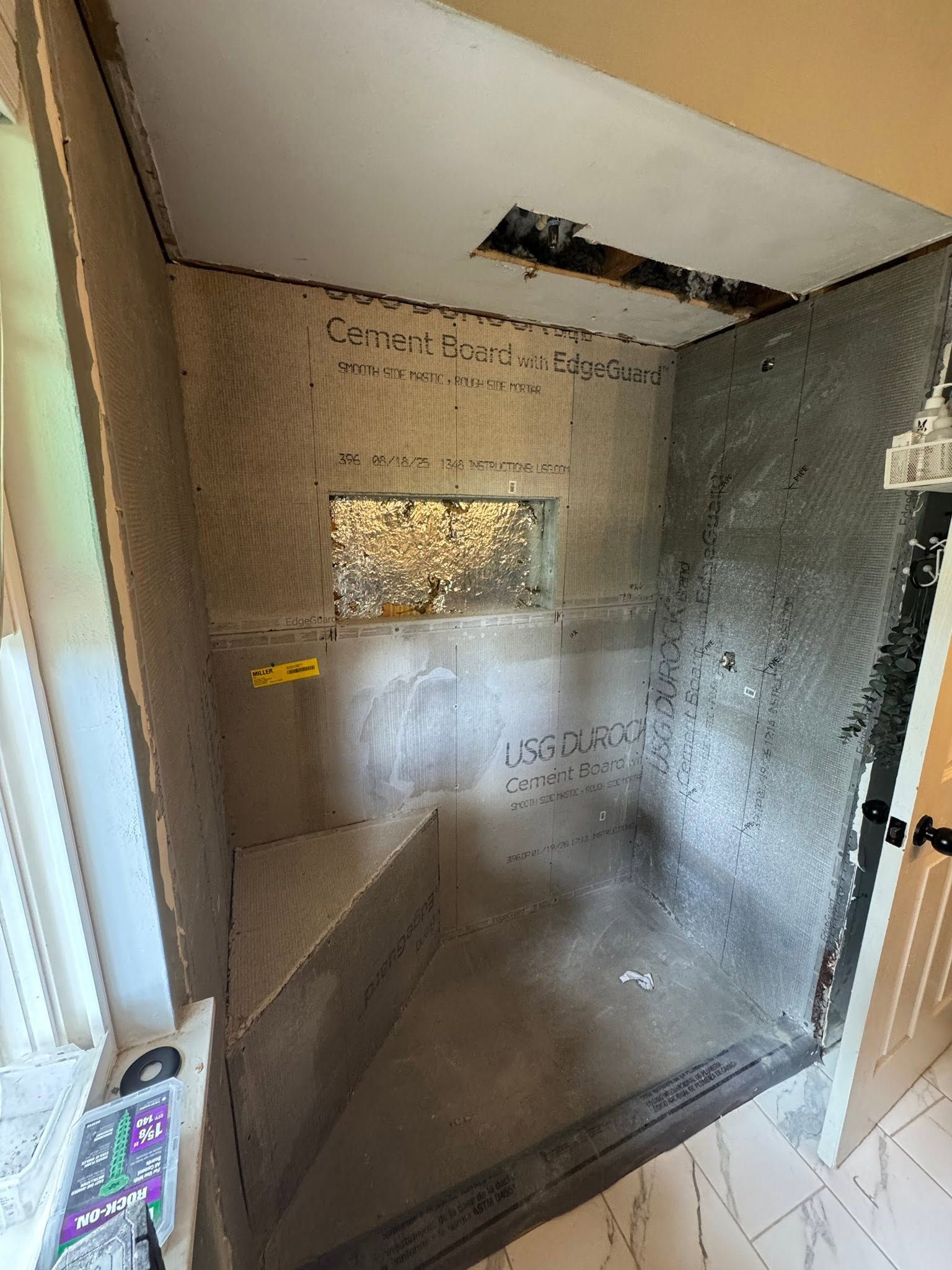 Small unfinished shower stall with bare concrete walls, a window, and an open door.