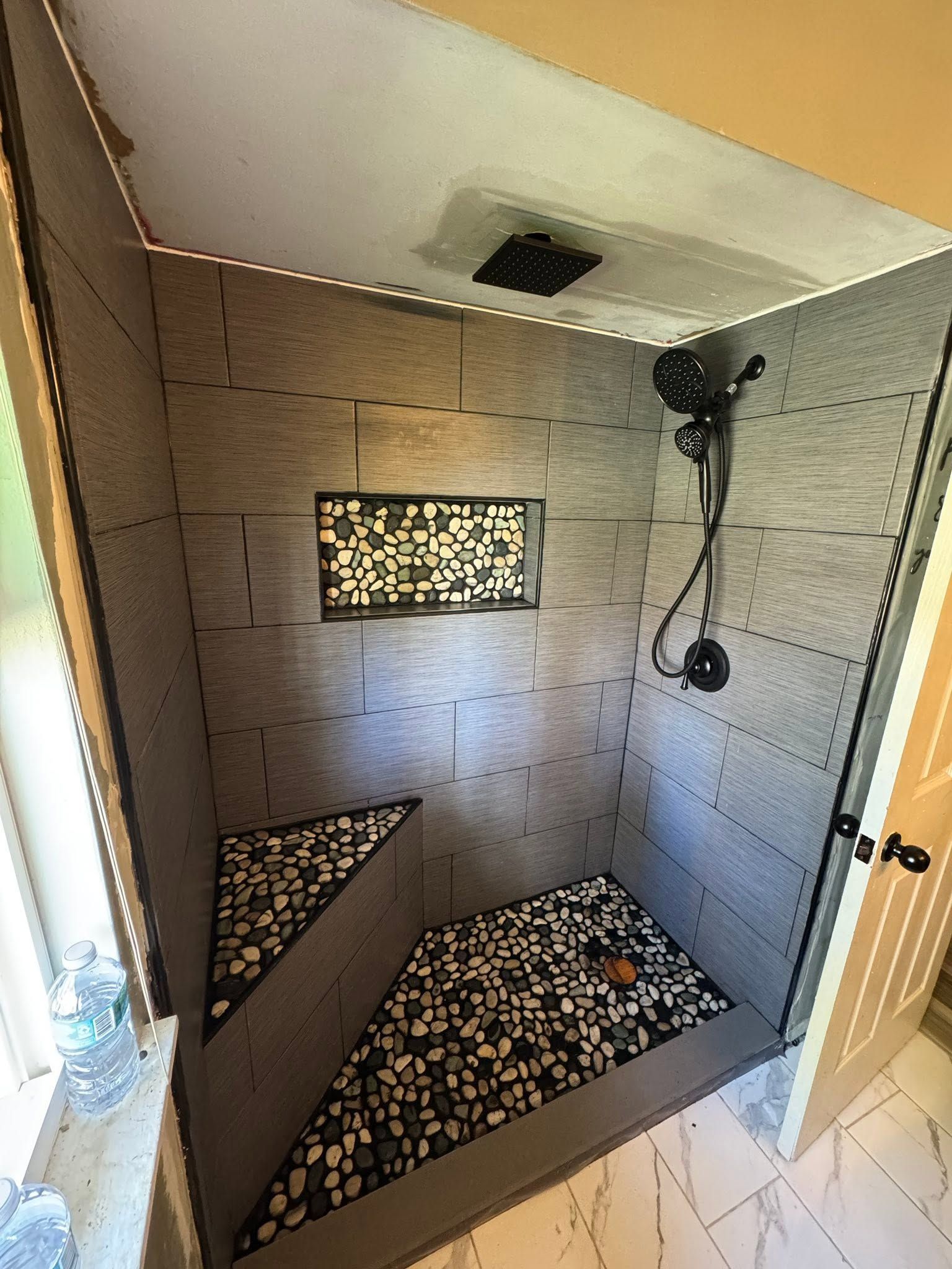 Small tiled shower stall with patterned floor, mosaic window, and wall-mounted showerhead.