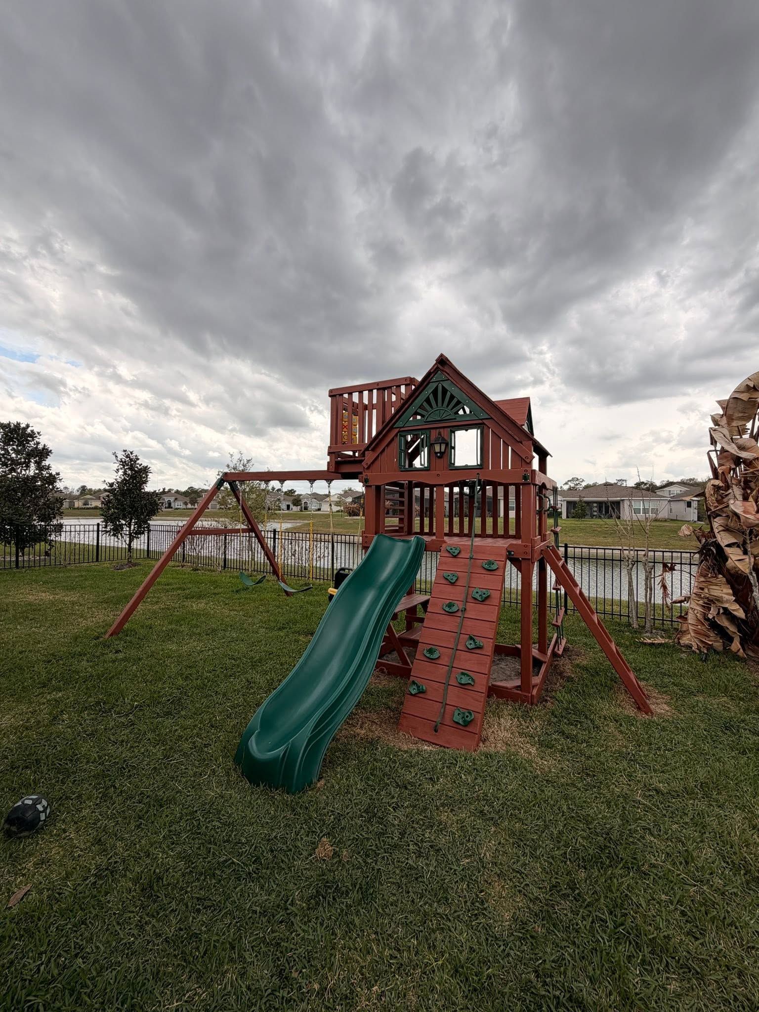 Children’s playground with green slide and red climbing structure under a cloudy sky