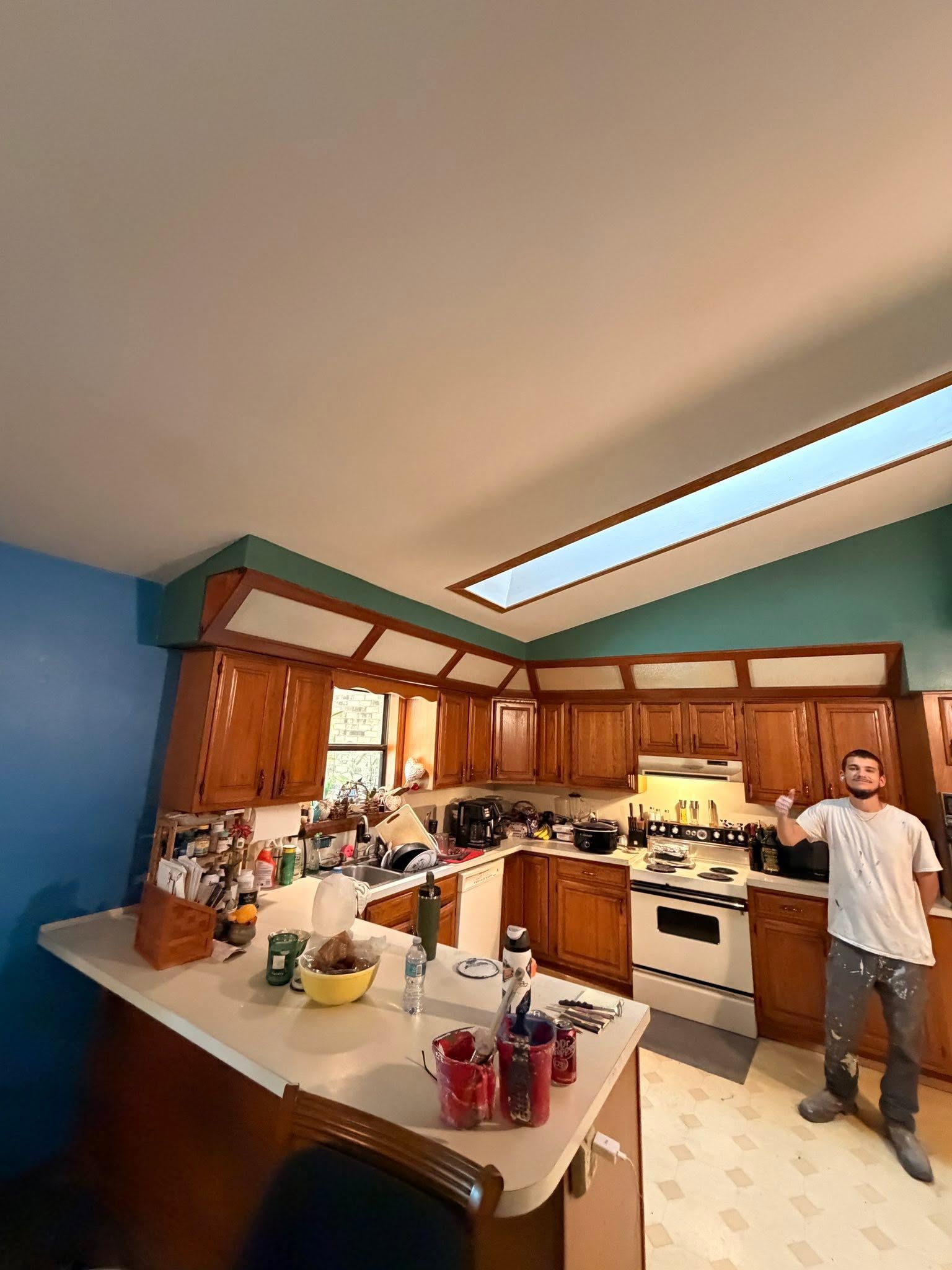 Kitchen with wooden cabinets, blue walls, white island, and a man standing near the stove under a skylight.