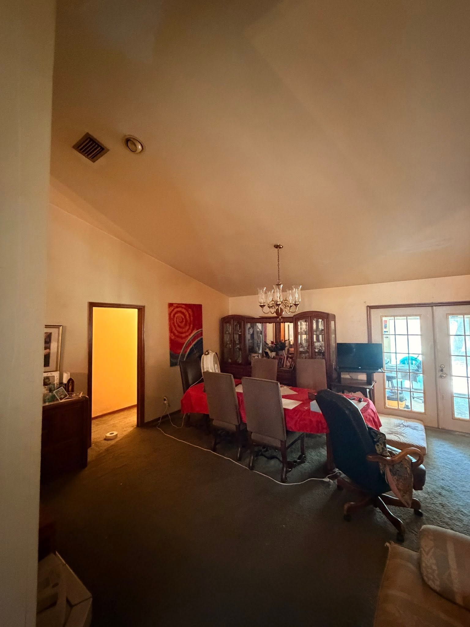 Dining room with chandelier, table and chairs, red curtains, and a person near the patio doors.