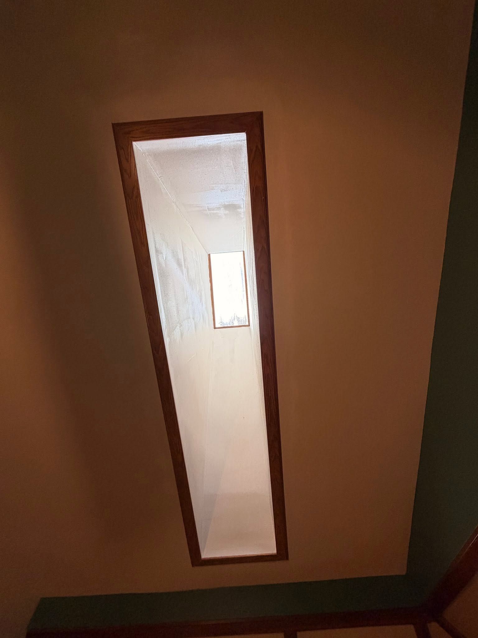 Narrow skylight in a brown ceiling, showing bright daylight through a tall rectangular opening