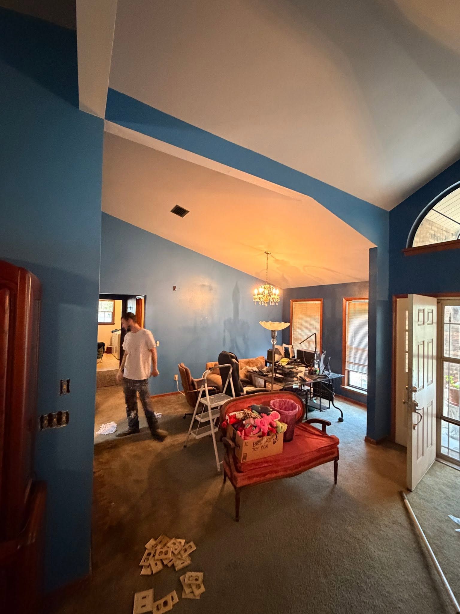 Blue-walled living room with sofa, chairs, table, and a man standing near the back door