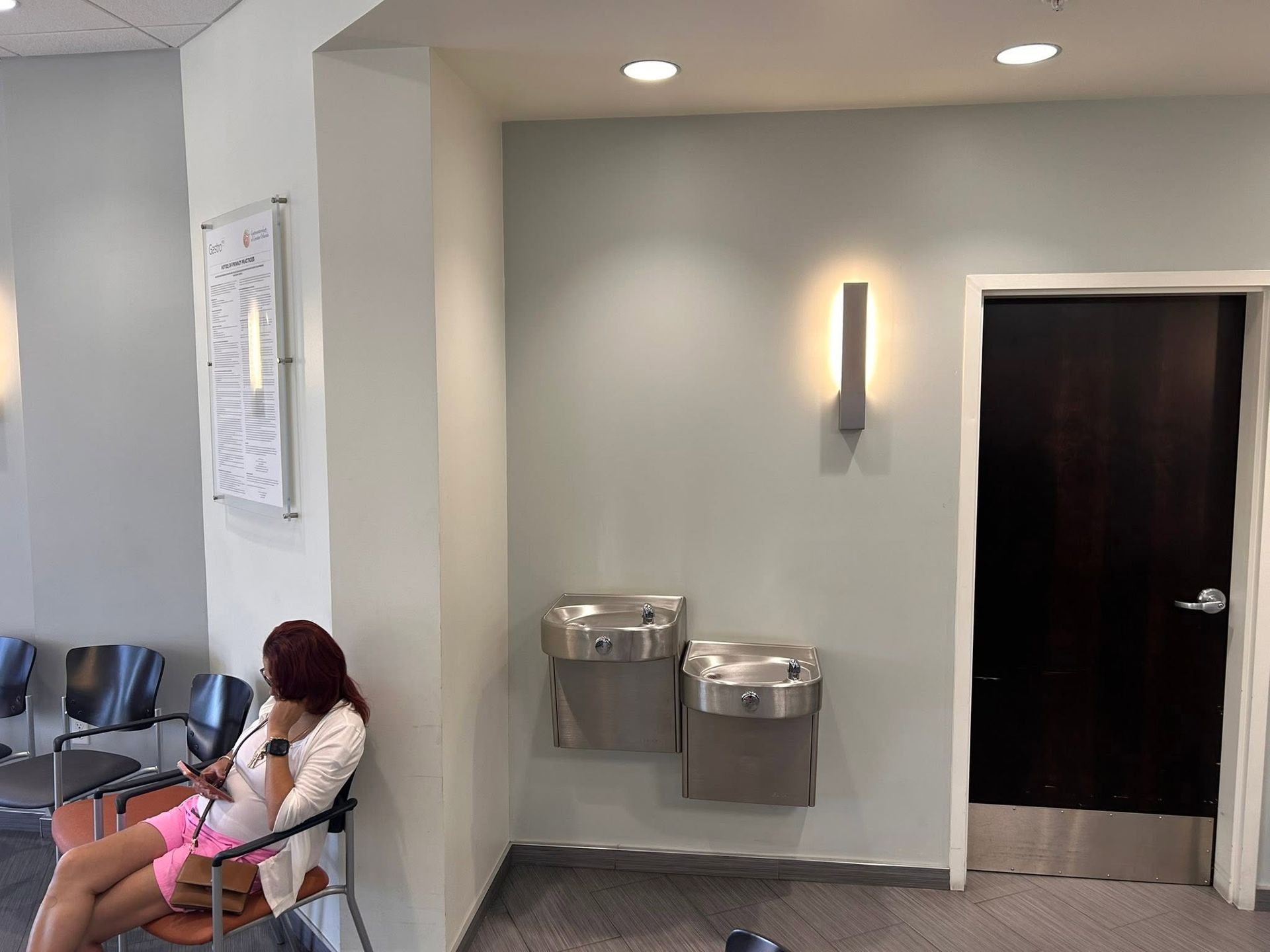 Waiting room with a seated person, water fountains, wall light, and a dark door