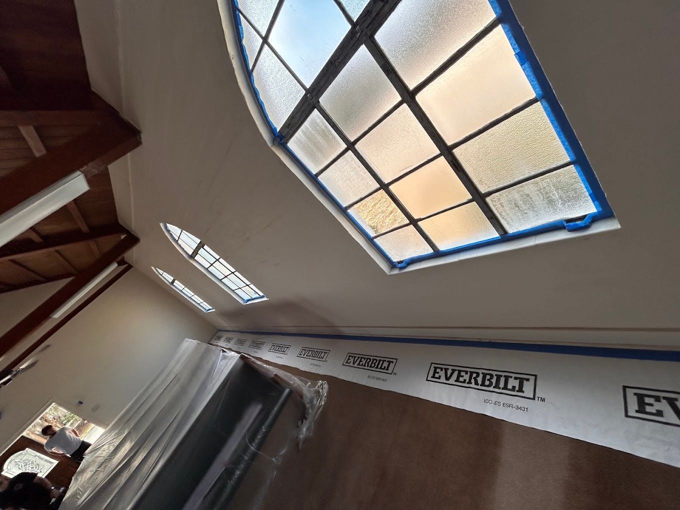 Tilted indoor ceiling with skylight, exposed beams, and plastic-covered window.