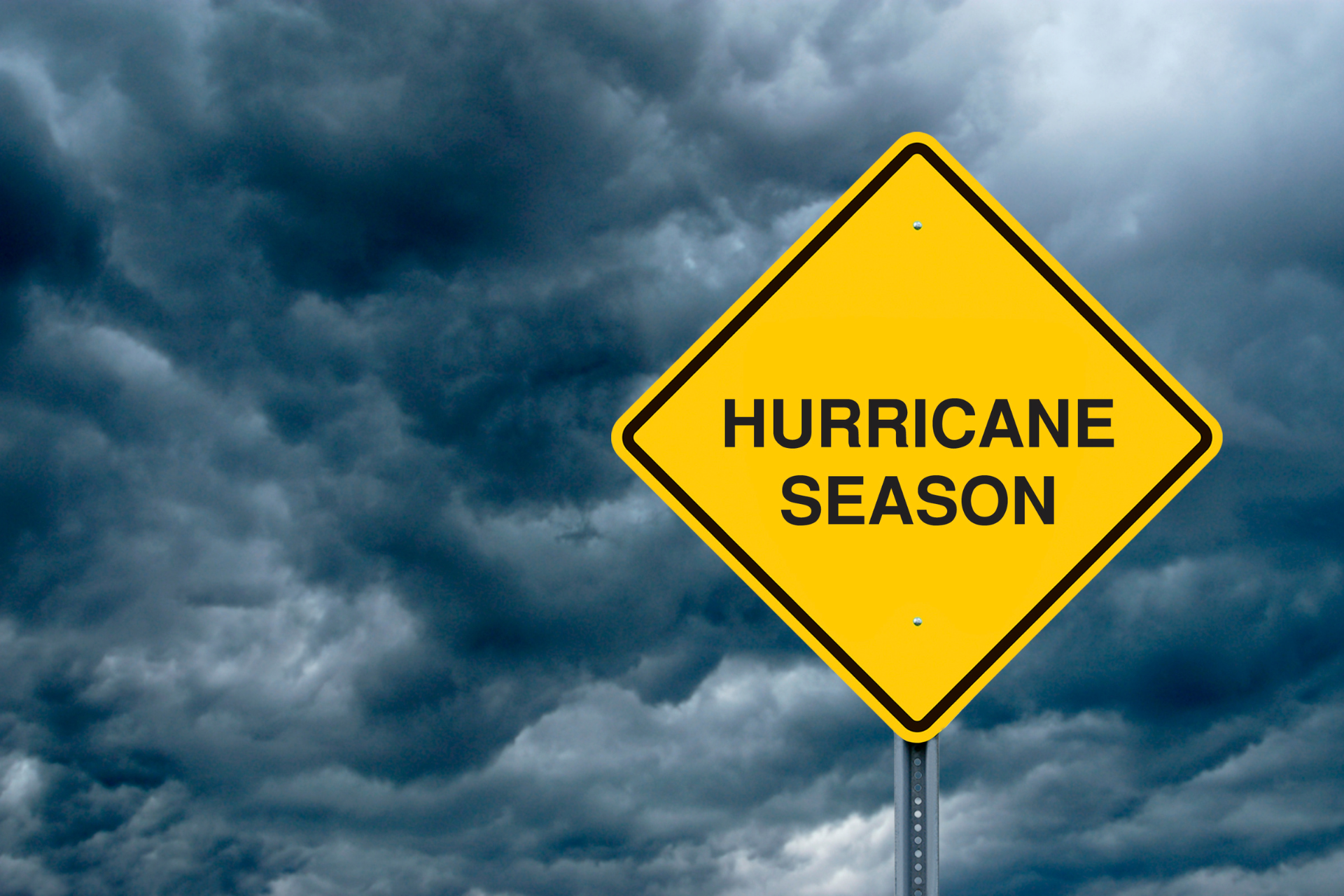 Yellow hurricane season warning sign against dark storm clouds
