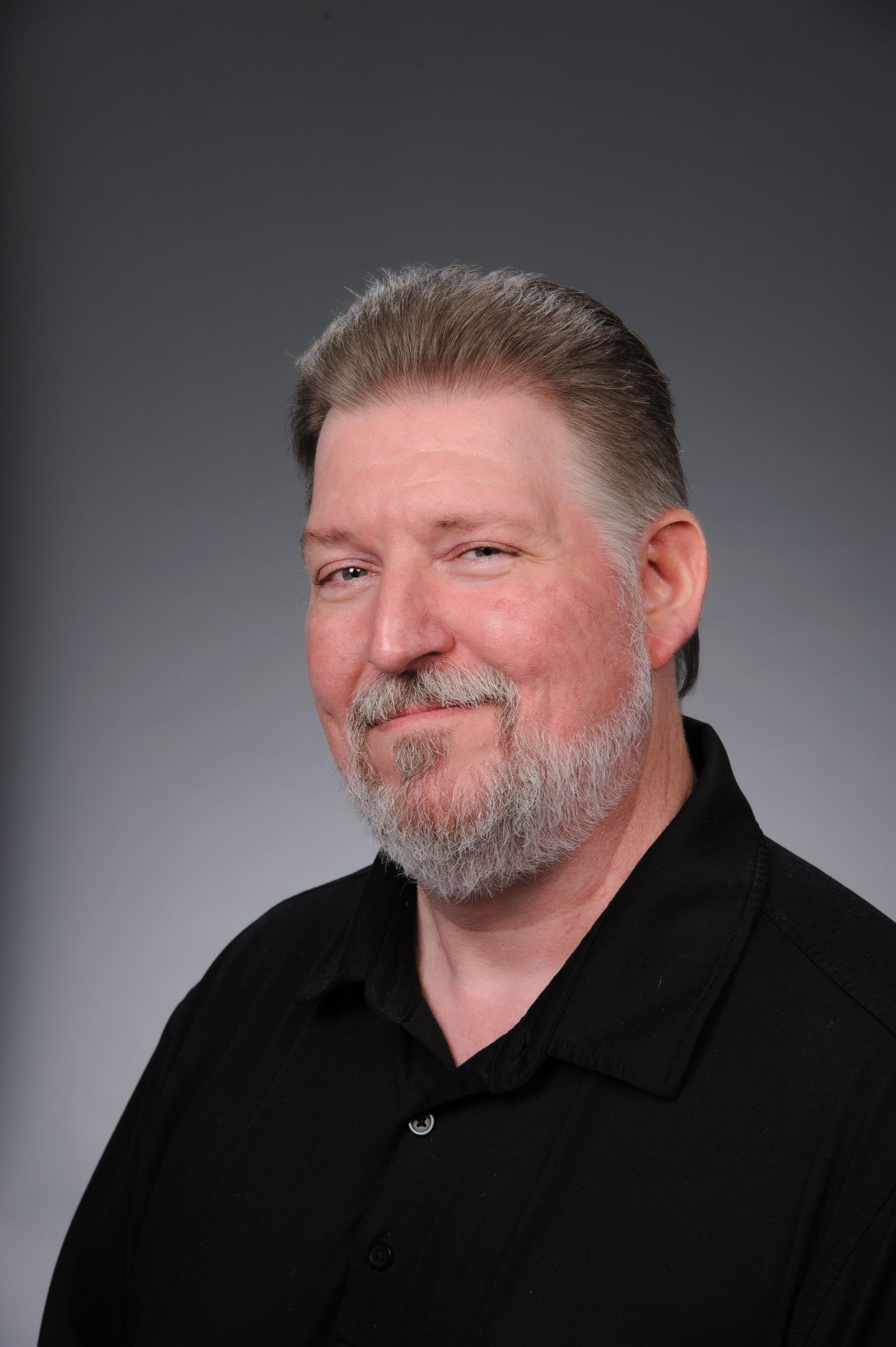 Portrait of a smiling man in a black shirt against a gray studio background