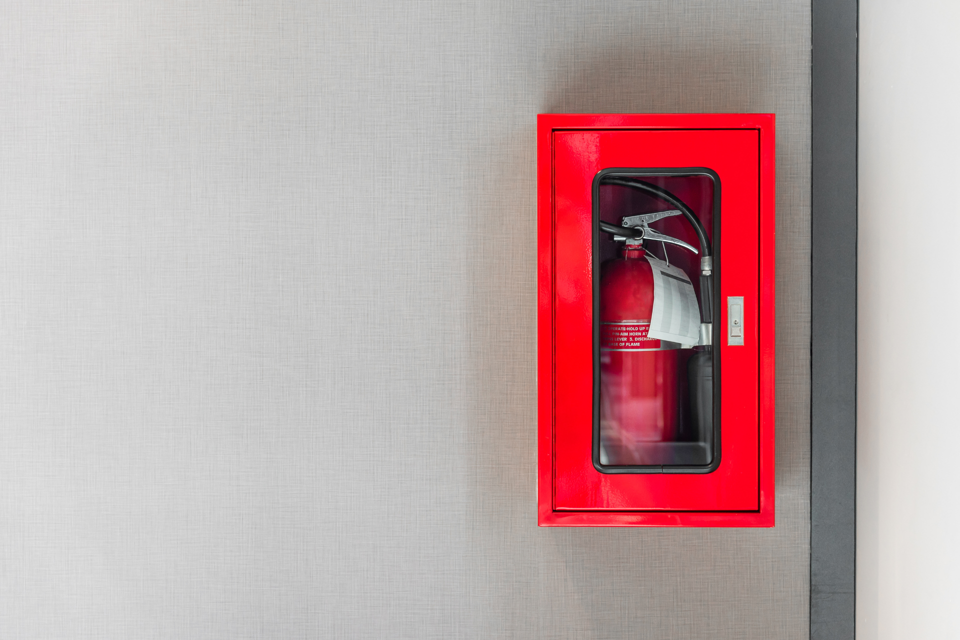 Red fire extinguisher cabinet mounted on a gray wall