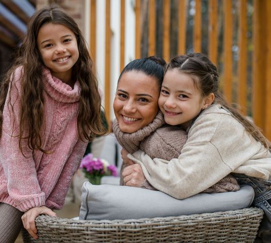 a mother and two daughters are posing for a picture while sitting on a wicker chair .