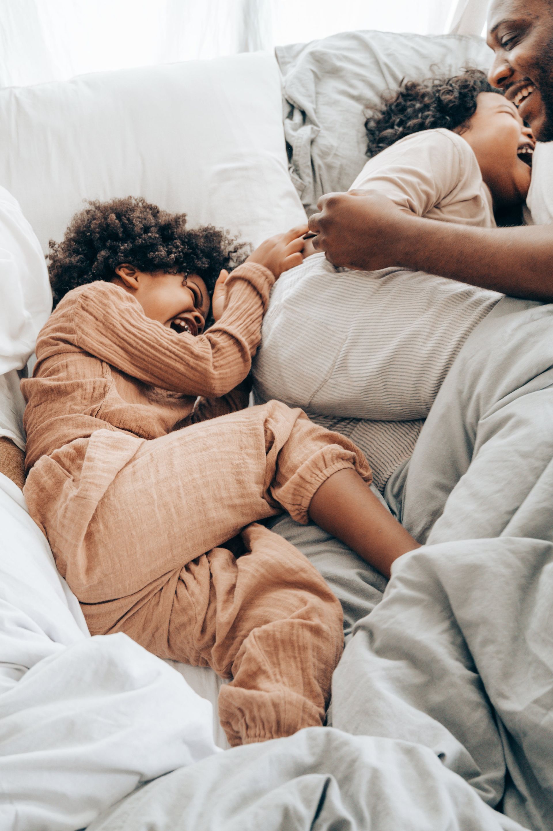 Two children sleeping on a white bed beside an adult, all covered with soft blankets