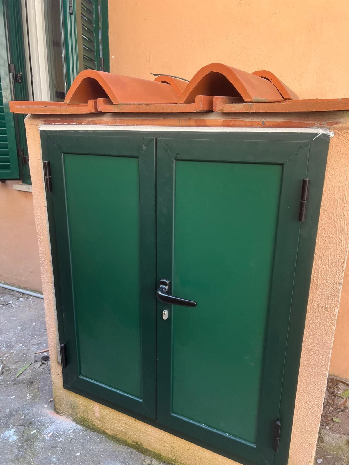 Doppie porte verdi in un recinto di stucco, sormontato da piastrelle di terracotta.