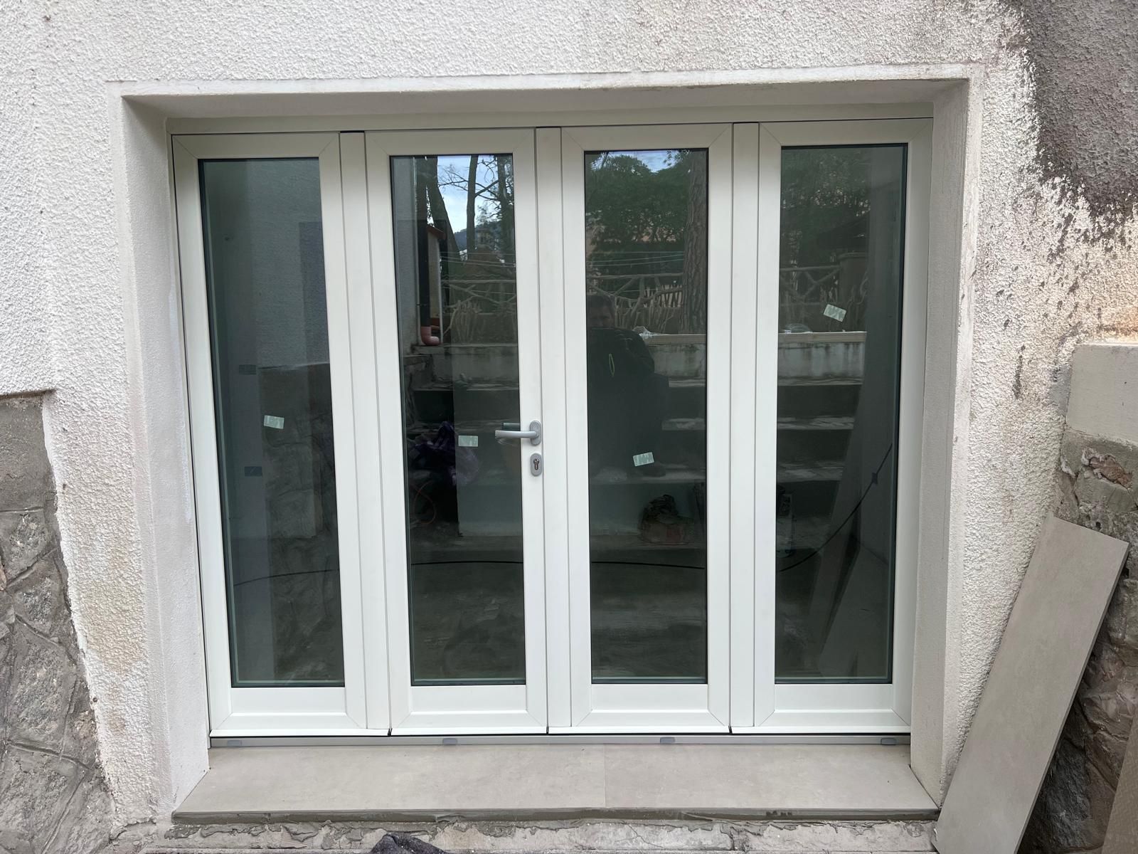 Le porte-finestre in vetro si aprono su un interno soleggiato e su una vista esterna. Telaio in legno marrone, vetro riflettente.
