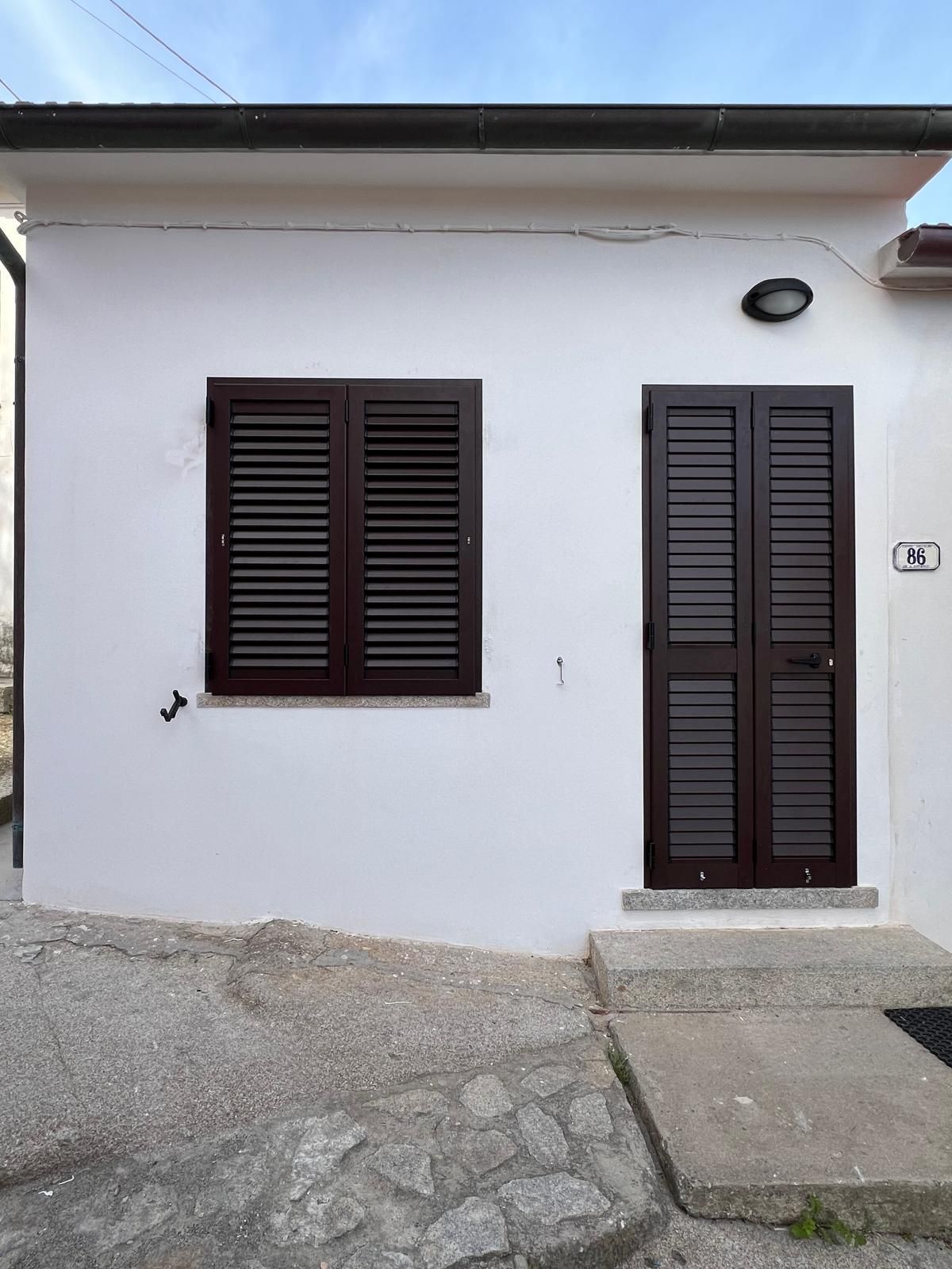 Edificio bianco con persiane marroni su finestre e porte. Gradini in cemento conducono all'ingresso.