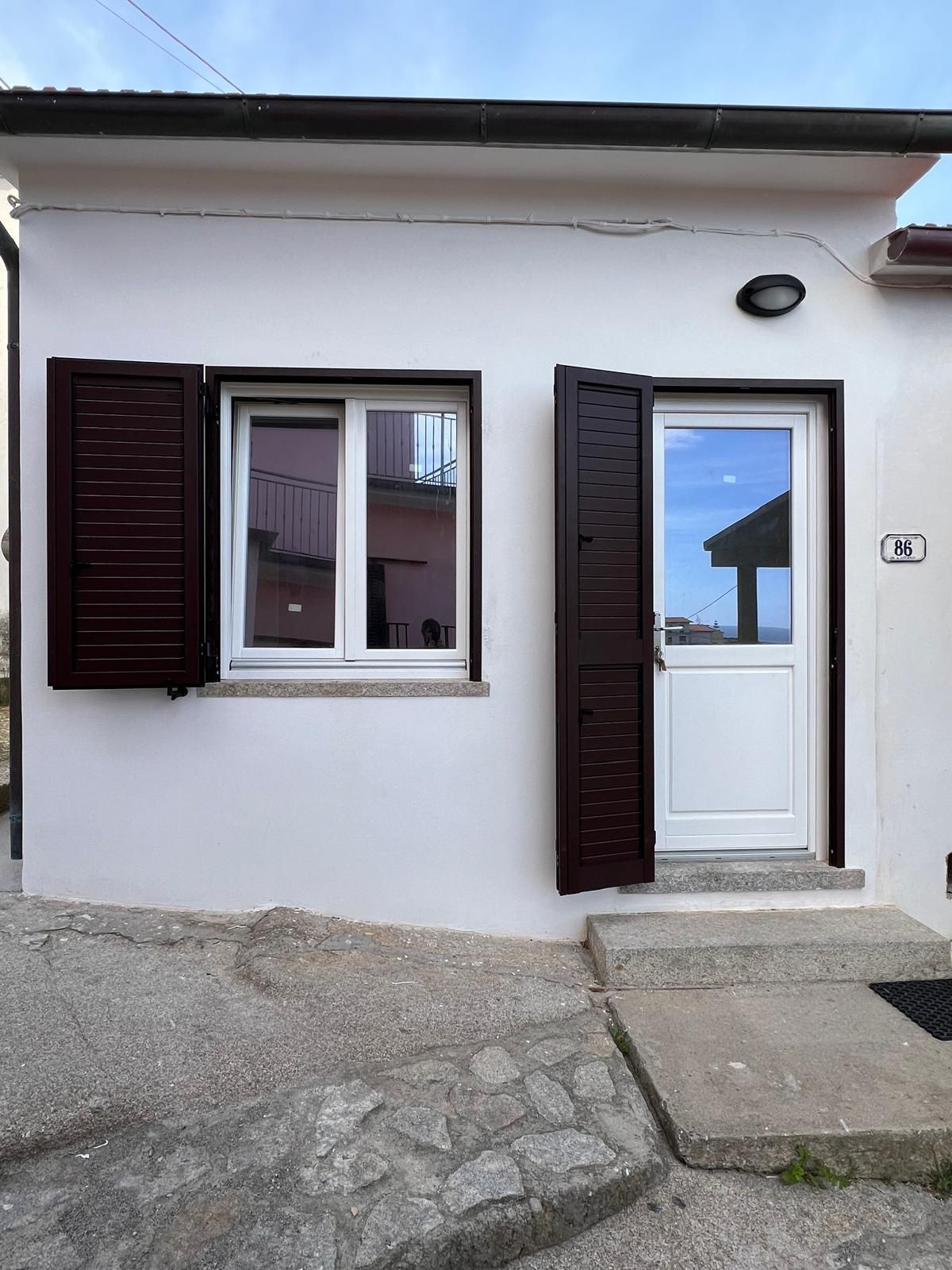Edificio bianco con persiane marroni, porta bianca e un piccolo gradino di cemento.