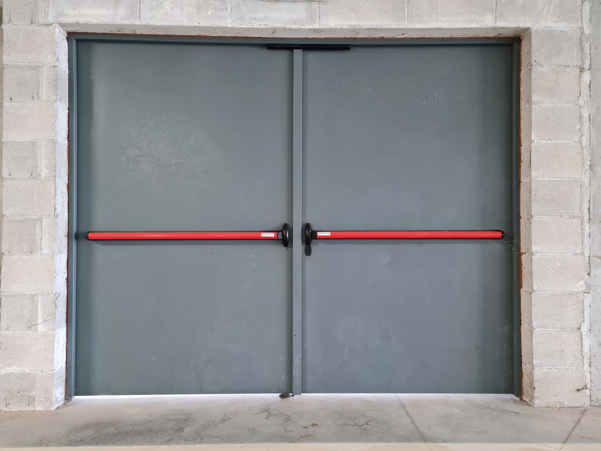 Porta a soffietto marrone scuro, parzialmente aperta, in un corridoio dalle pareti bianche. Vista su una stanza arredata.
