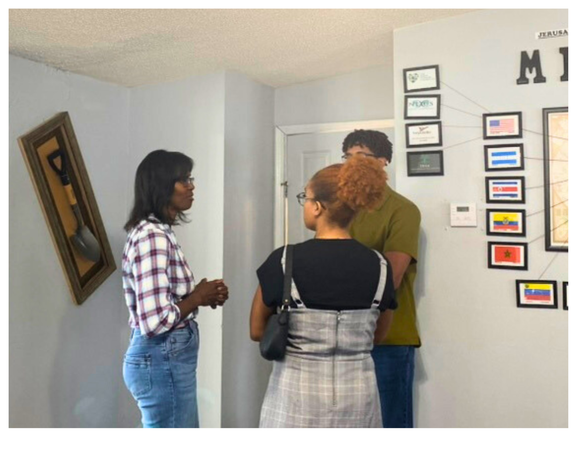 Three people talking in a bright room with framed signs on the wall.