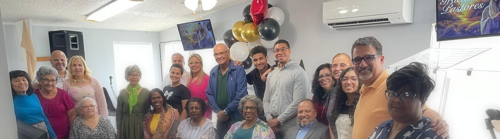 Grupo de personas posando en el interior de una celebración, sonriendo entre globos y adornos de fiesta.