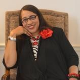 A woman is sitting in a chair with a red rose in her hair.
