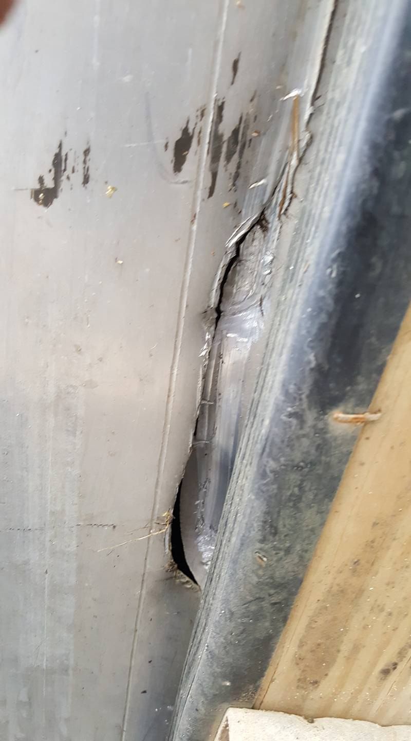Close-up of a damaged metal surface with a crack and hole near a black edge.