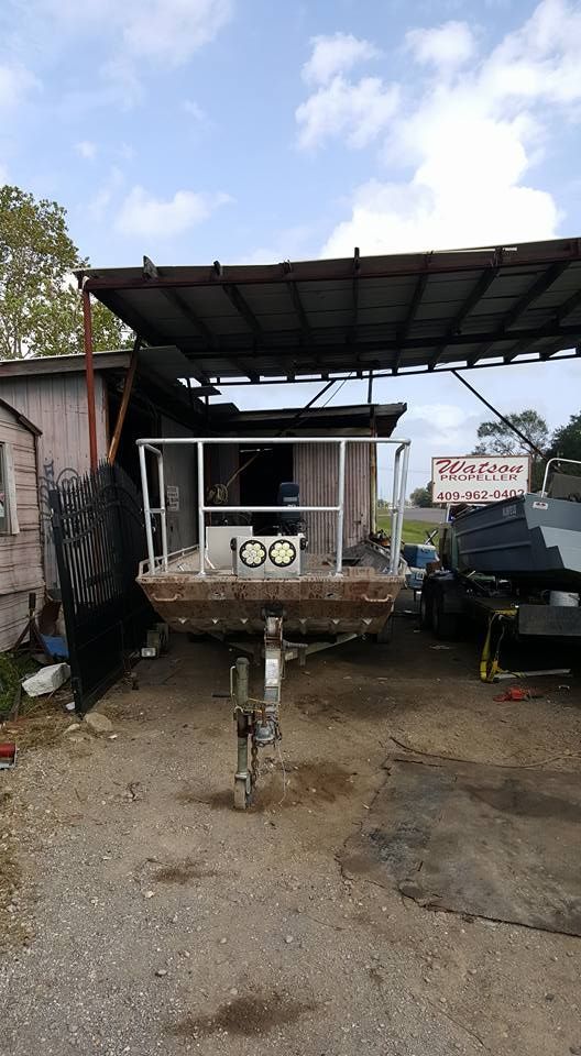 Boat trailer with welded metal frame, under a metal awning outside a building.