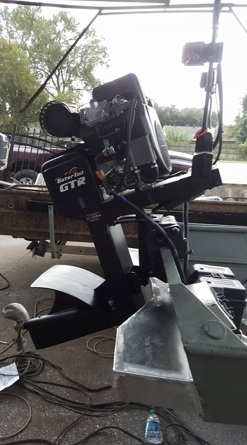 Mud motor attached to a boat. The motor is black, the boat is green, outdoors.