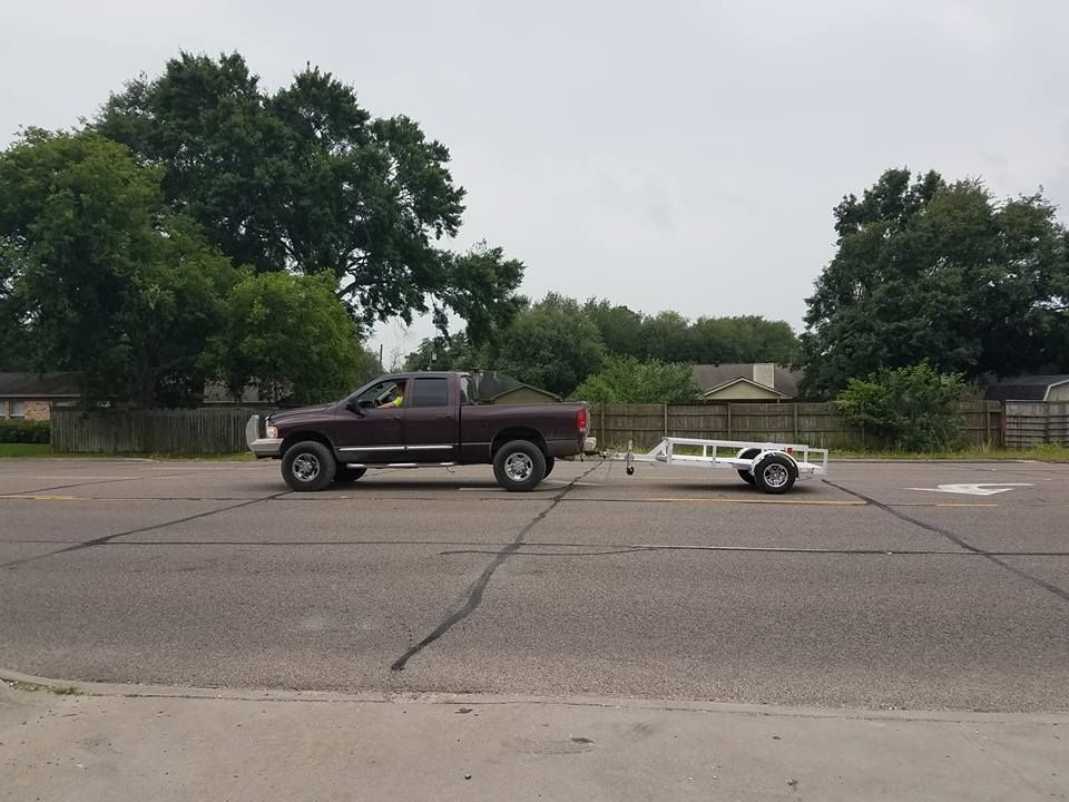 Dark brown pickup truck towing a white trailer in a paved lot, overcast sky, trees in the background.