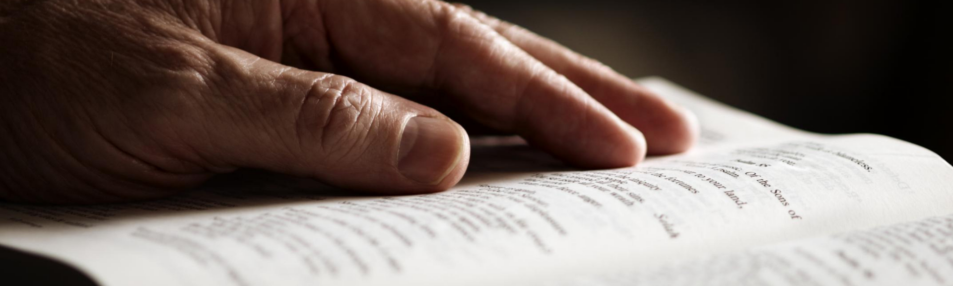 Hand resting on an open book, fingers touching printed text under warm light
