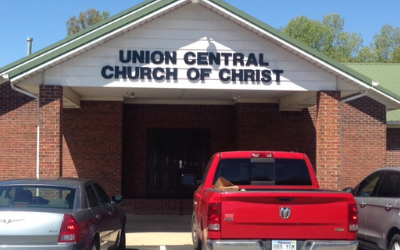 Union Central Church of Christ brick entrance with parked cars, including a red pickup truck, in front.