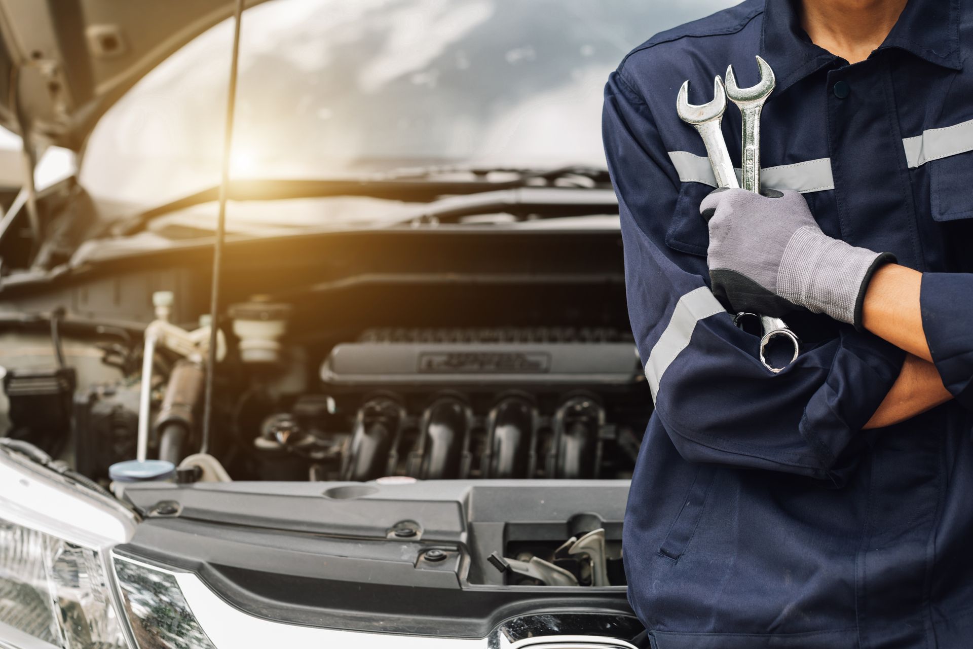 Mechanic in blue coveralls with wrench standing beside open car hood in a garage