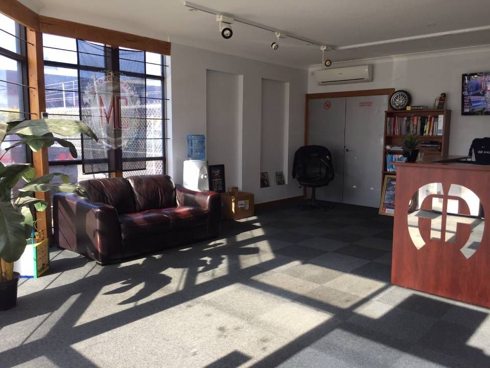 Bright waiting room with a brown sofa, front desk, large windows, and sunlit floor shadows