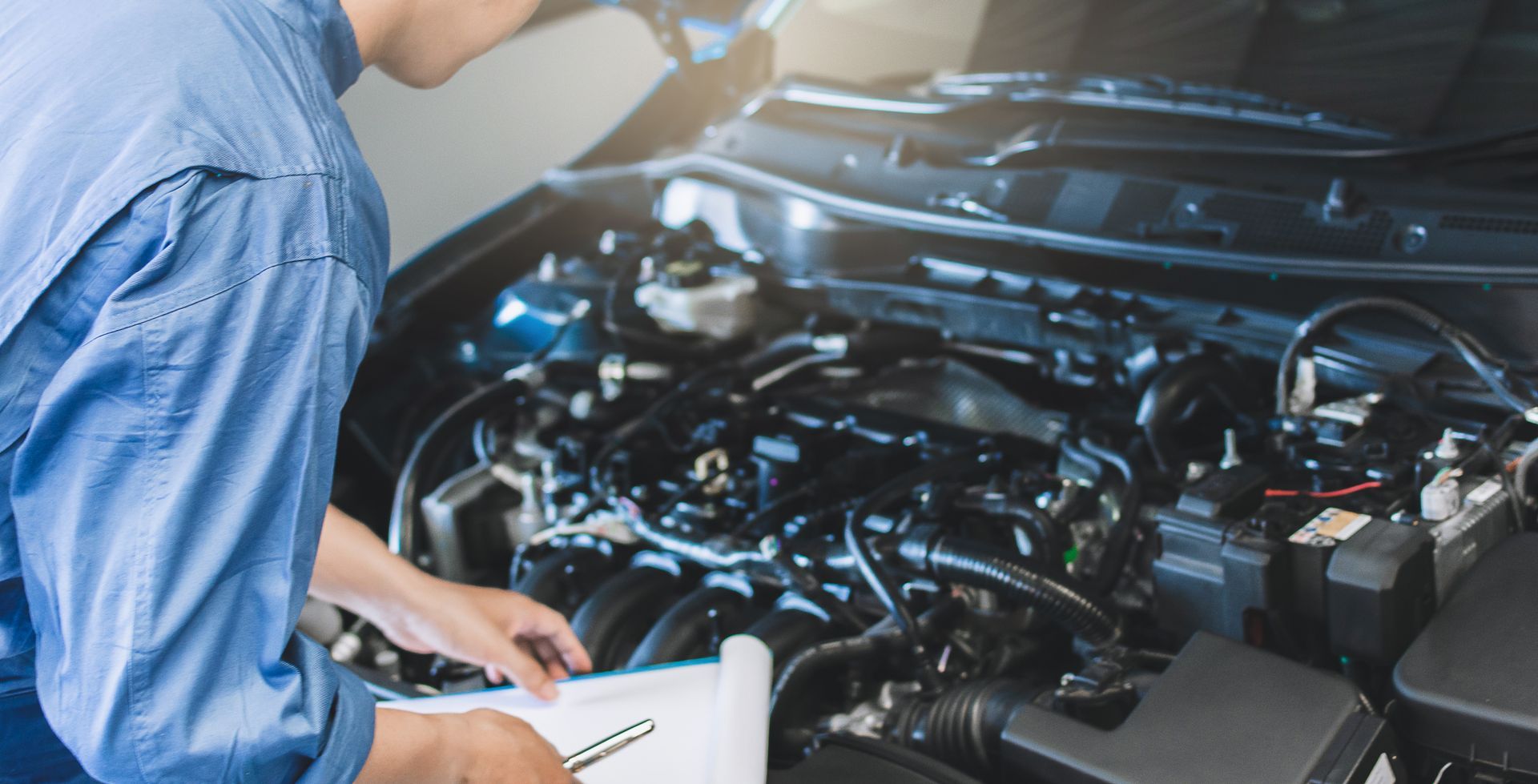 Mechanic inspecting car engine with a clipboard in a garage