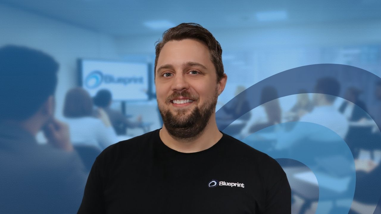 Man smiling, wearing black shirt with logo, in classroom setting with