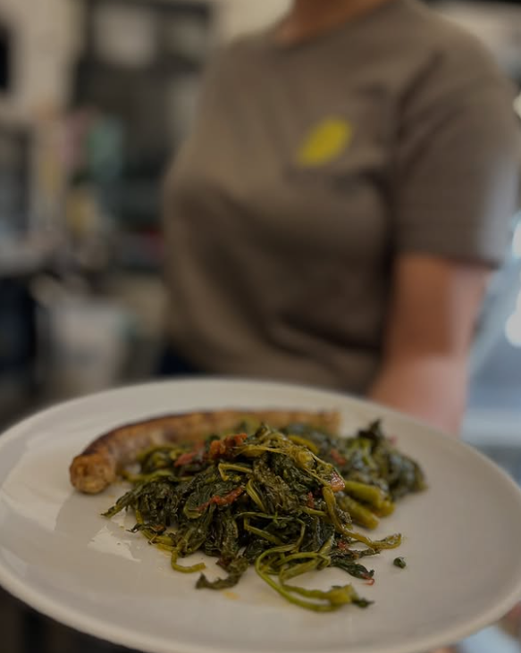 Persona che tiene in mano un piatto con salsiccia e verdure verdi.