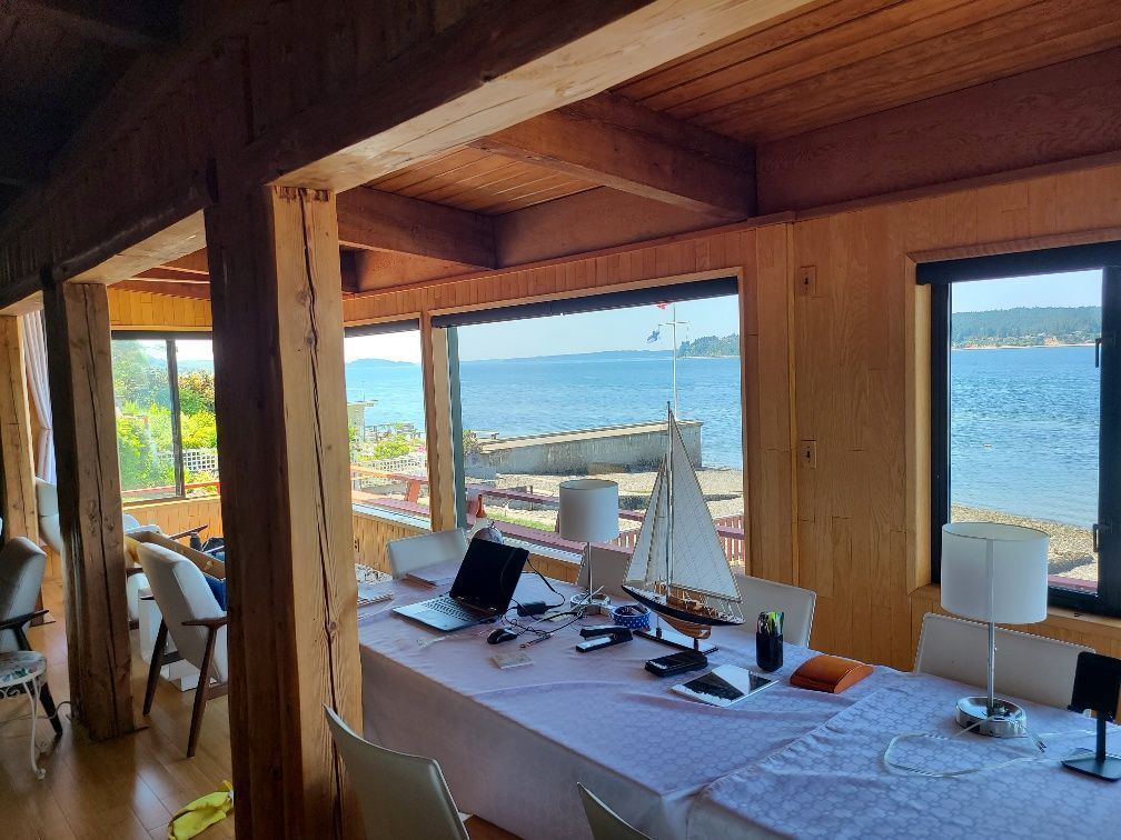 Interior room with a long table overlooking the ocean, wooden beams, and a sailboat model.