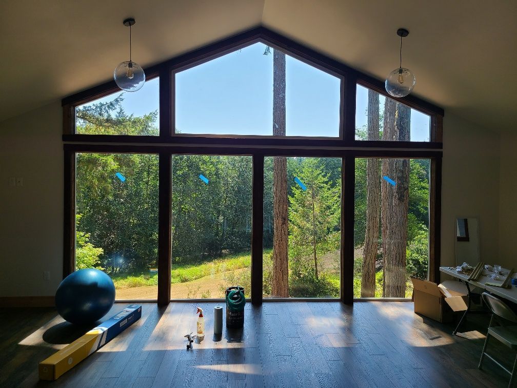 Room with large windows framing a view of trees and blue sky. Wooden trim, dark floor, and blue exercise ball.