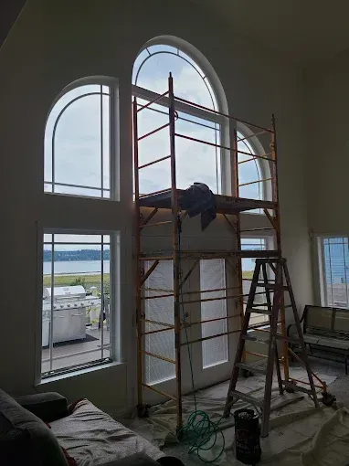 A high-ceiling room with arched windows. Scaffolding is set up near doors, with a ladder.