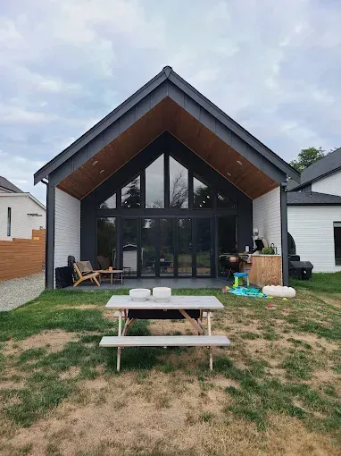 Backyard view of modern home with black trim, large glass doors, and a picnic table on the lawn.