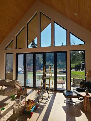 Interior view of a modern house with large windows and a sunny backyard visible.