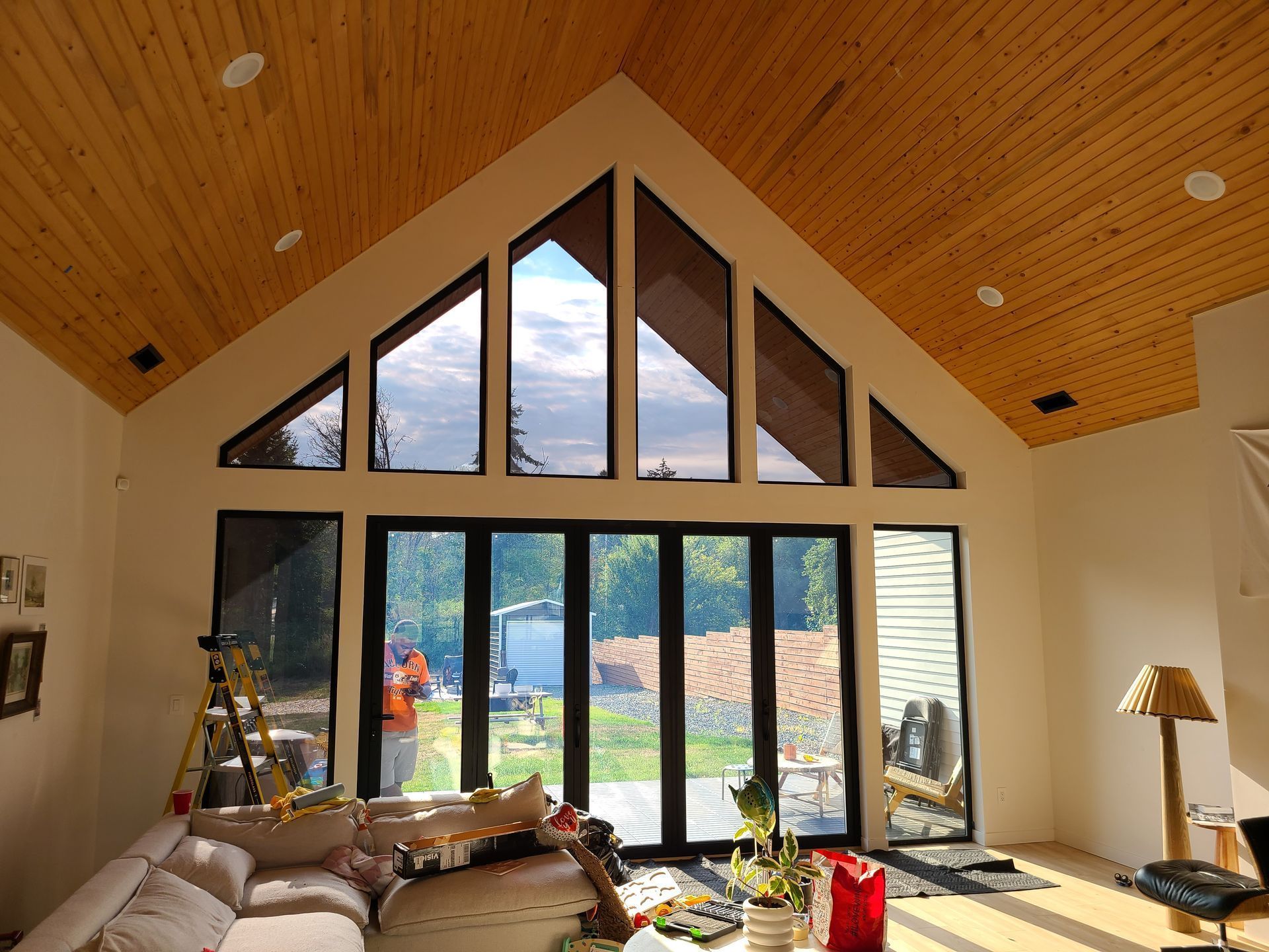 Living room with high ceilings, large windows overlooking a yard, a person visible outside.