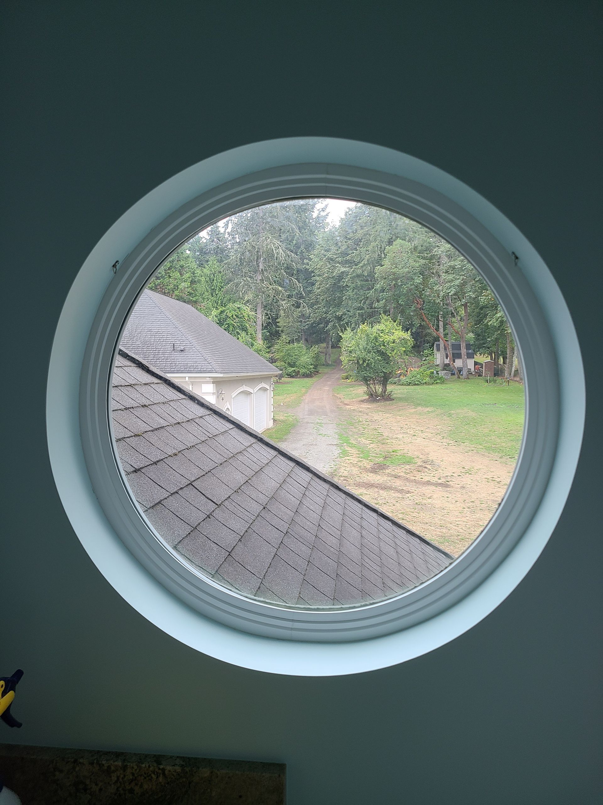 Round window with a view of a yard and a roof.