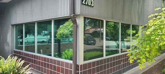Corner of a building with large windows; the building has a brick and metal facade, and green tinted windows.