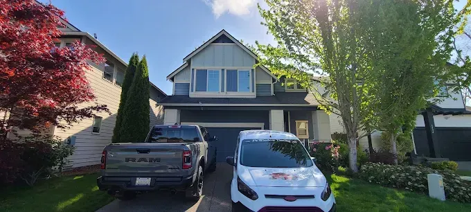 A house with a dark gray garage, a truck, and a white van parked in the driveway, trees surround the house.
