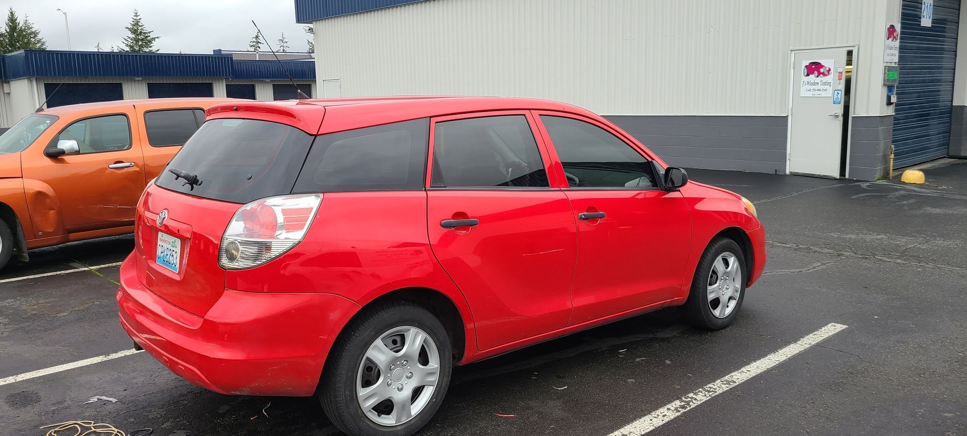 A red Toyota Matrix parked in a lot on a cloudy day. An orange SUV is parked next to it.