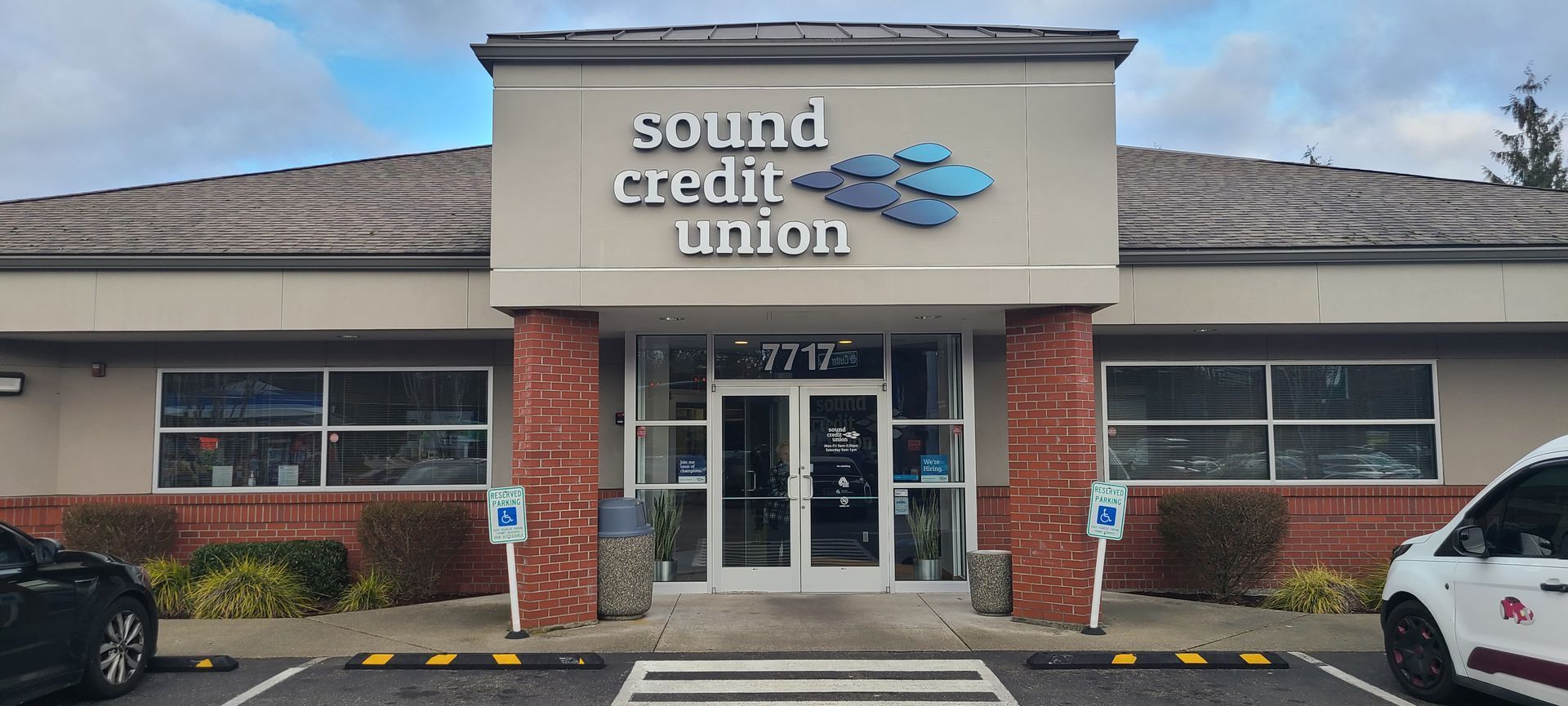 A Sound Credit Union building entrance, with brick pillars and a blue logo, under a cloudy sky.