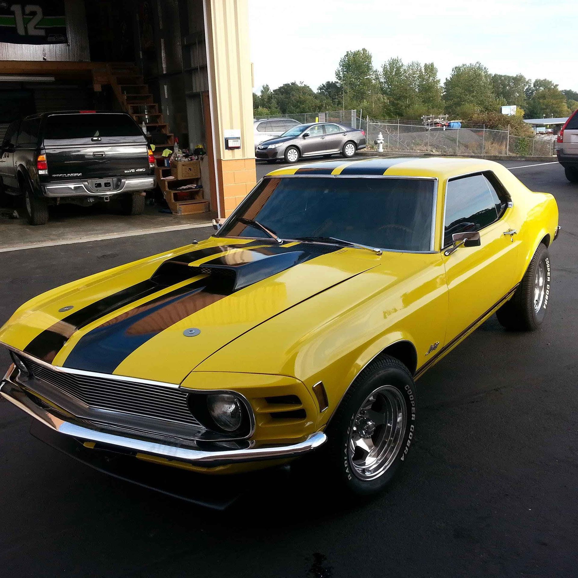 Yellow classic Ford Mustang with black racing stripes parked outside a garage.