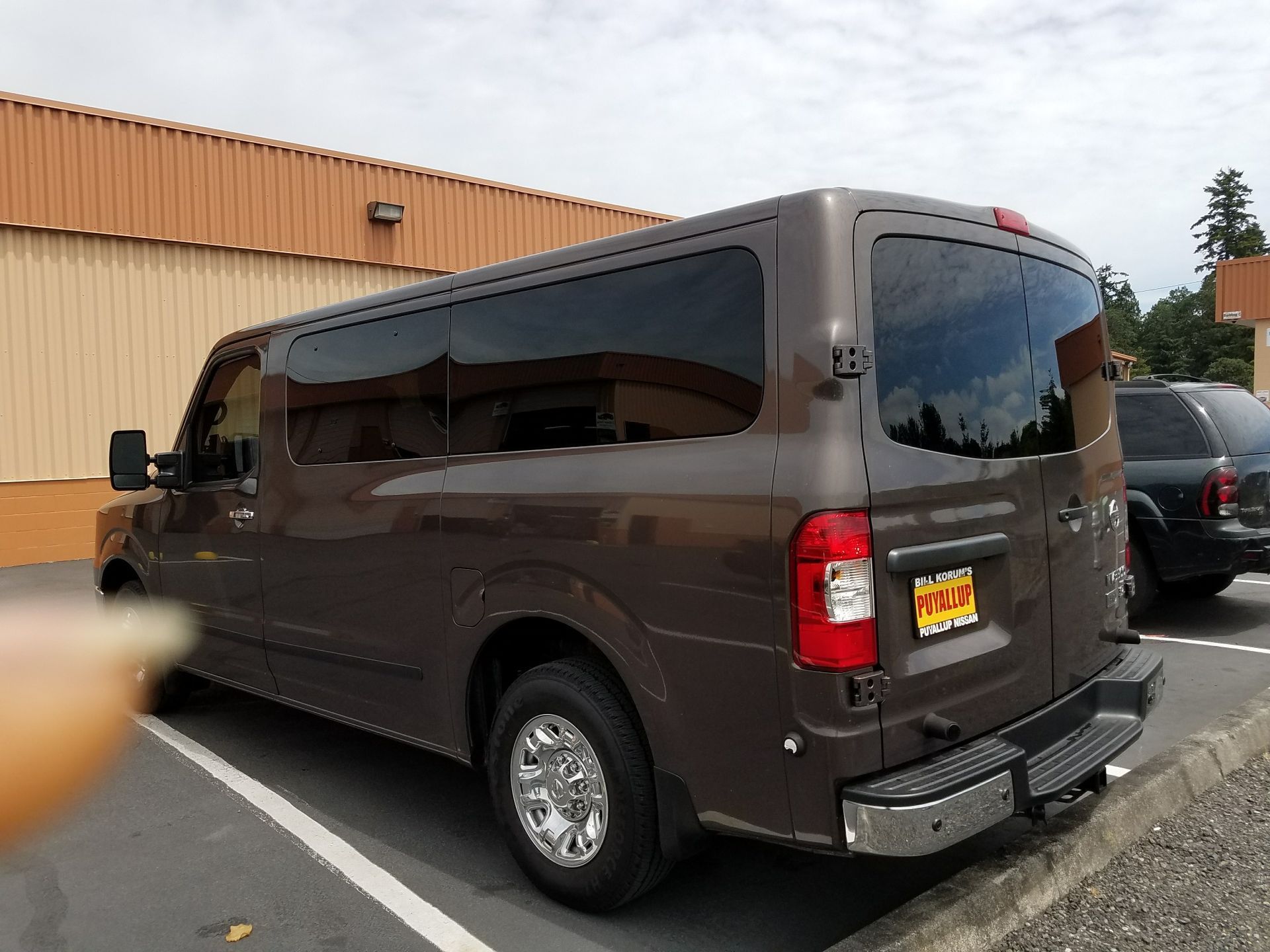 Brown passenger van parked outdoors, tinted windows, chrome wheels.