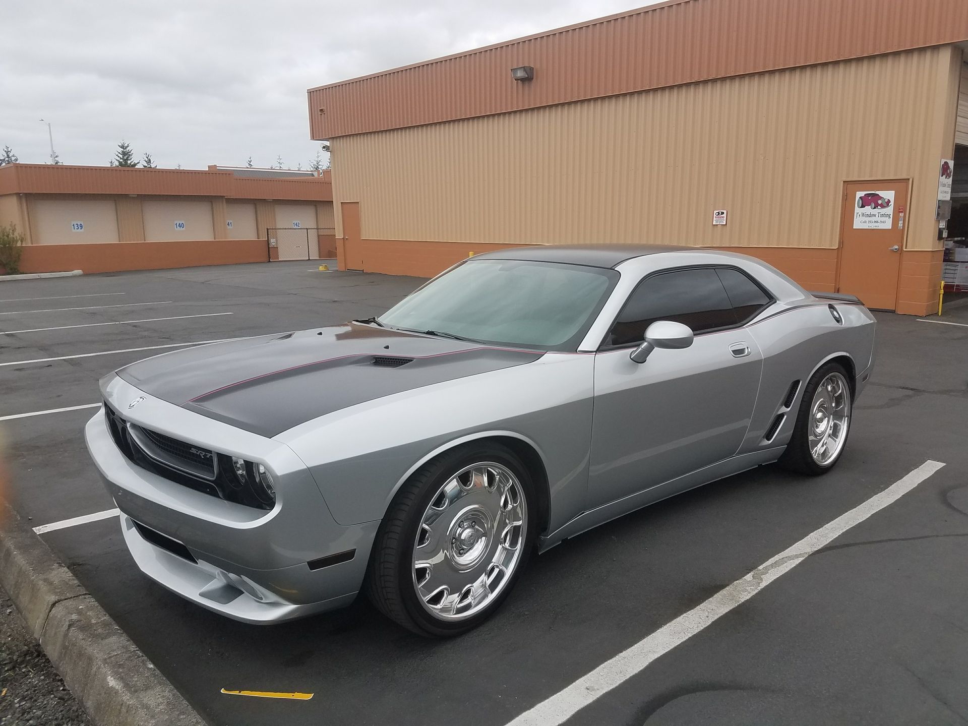 Silver Dodge Challenger with black hood, parked outside a building.