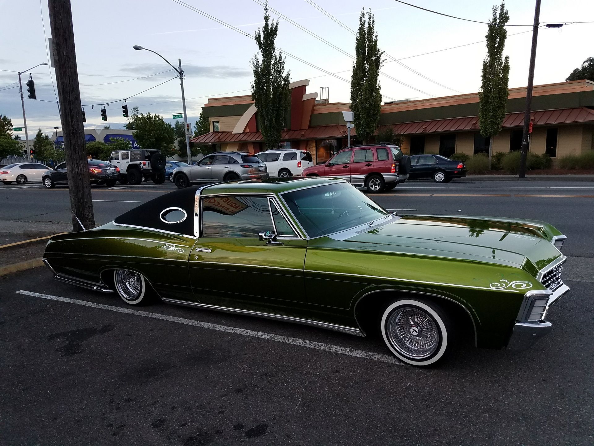 Green classic car parked on a city street, lowrider style.
